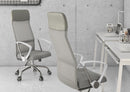 A modern office features two Silla Economalla Gris office chairs, a minimalist white desk with laptops, textured concrete walls, and shelves of magazines in the background.