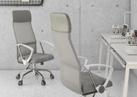 A modern office features two Silla Economalla Gris office chairs, a minimalist white desk with laptops, textured concrete walls, and shelves of magazines in the background.