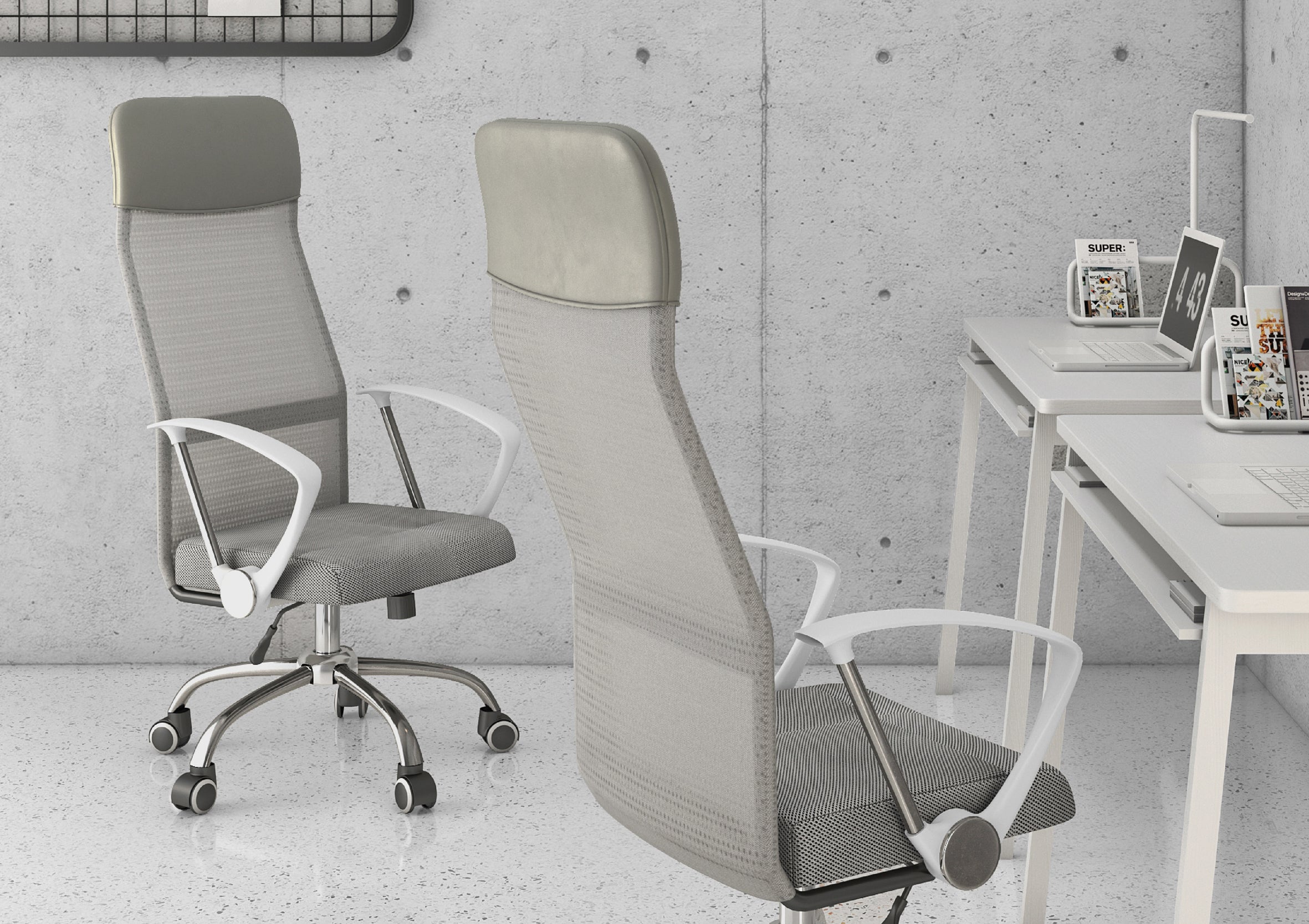 A modern office features two Silla Economalla Gris office chairs, a minimalist white desk with laptops, textured concrete walls, and shelves of magazines in the background.